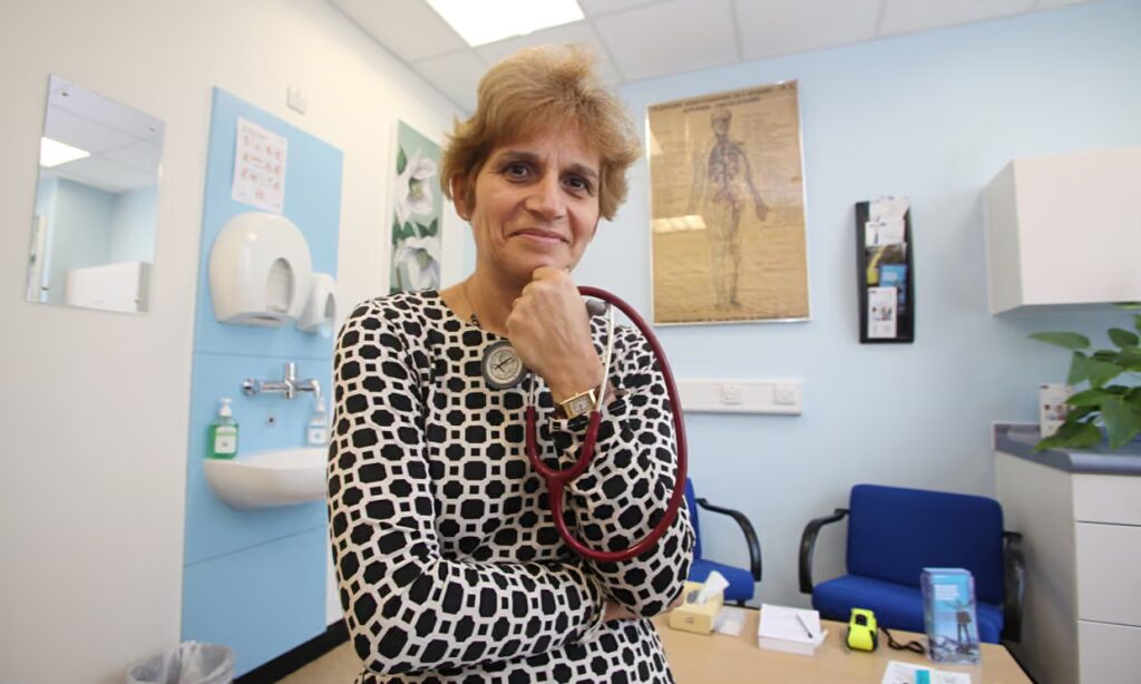 Clare Gerada sitting in a medical office wearing a black and white shirt with a stethescope in her hand