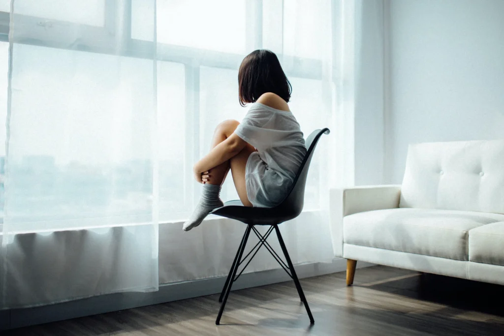 A young female sitting on a chair hugging her legs, feeling lonely and isolated